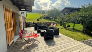Eine Holzterrasse mit Gartenmöbeln, Blick auf eine grüne Landschaft und eine Steinmauer.