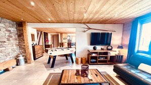 Ein gemütliches Wohnzimmer mit einem Kicker, einem Couchtisch, einer Couch und einem an der Wand befestigten Fernseher.