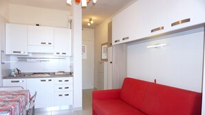 Cozinha moderna com armários brancos e um sofá vermelho na sala.