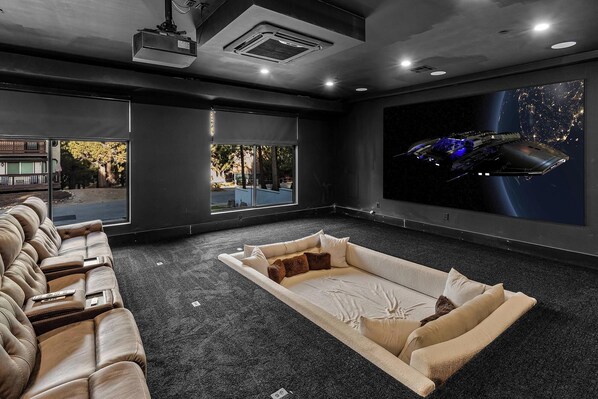 A home theater room with a large screen, reclining sofas, and a carpeted floor.