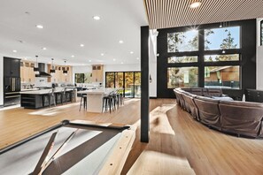 A modern kitchen with a central island, bar seating, and large windows. - The Getaway Club: Exclusive & Luxurious 7 Bed 7 Bath Retreat! Hot Tub! Pool Table! Shuffleboard! Air Hockey! Ping Pong! High Tech Theater w/ Theater Seating + Lounge Pit! Master Suite w/ Projection Screen! (Big Bear Lake)