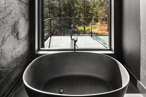 Et moderne badeværelse med et fritstående badekar, et vindue med udsigt til en balkon og en væg med struktur.