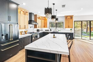 A modern kitchen with a large island, dark cabinetry, and a view to the outdoors.