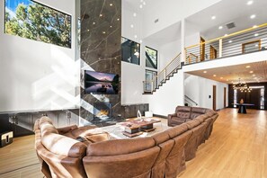 A spacious living area with a fireplace, leather sofas, and a large TV screen. - The Getaway Club: Exclusive & Luxurious 7 Bed 7 Bath Retreat! Hot Tub! Pool Table! Shuffleboard! Air Hockey! Ping Pong! High Tech Theater w/ Theater Seating + Lounge Pit! Master Suite w/ Projection Screen! (Big Bear Lake)