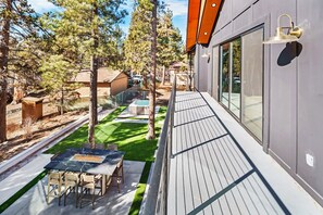 A modern outdoor deck with a dining table and chairs, surrounded by a well-maintained lawn and trees.