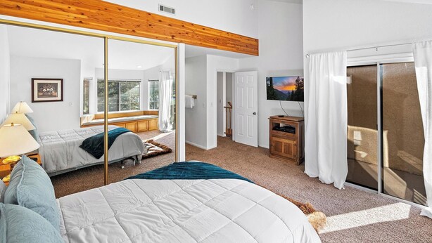 A bedroom with a large bed, a desk, a TV, and a sliding glass door to a balcony.