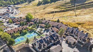 A residential area with houses, a tennis court, and a hilly landscape.