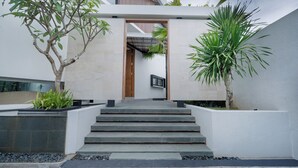 A modern house with a staircase leading to a wooden door, surrounded by potted plants and a white wall. - Uma Namu Villa by Betterplace (Canggu)