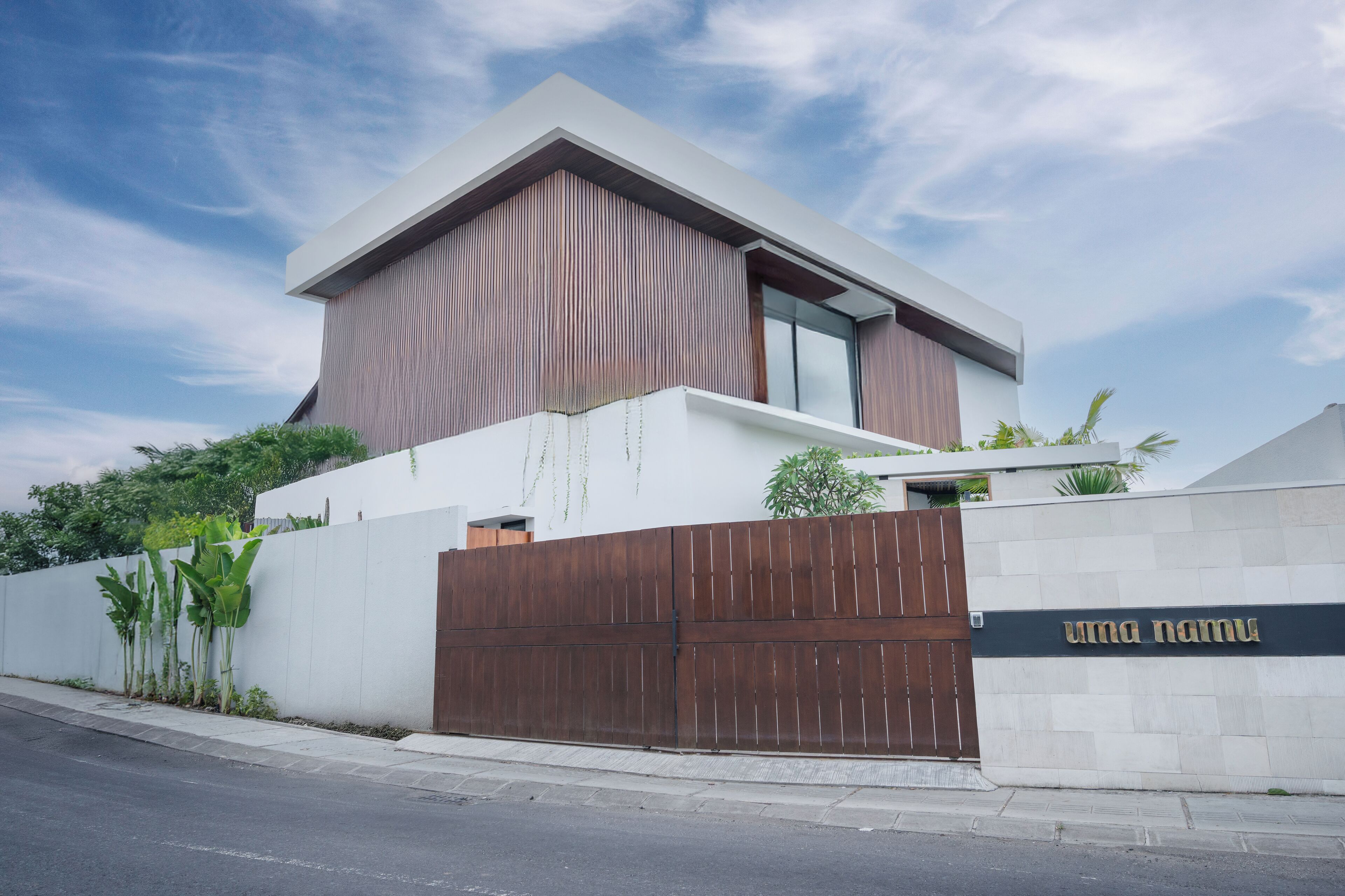 A modern two-story building with a large wooden gate, a white facade, and a sign that reads "uma namu".
