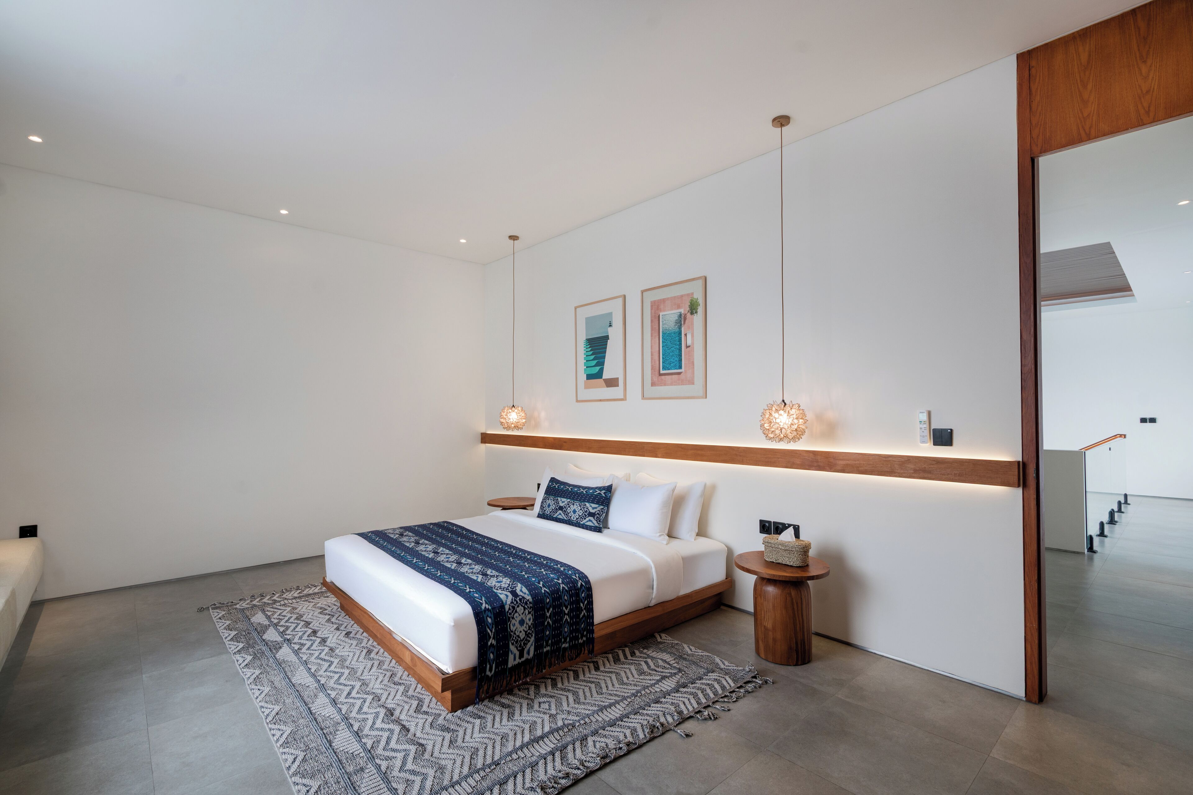 A modern bedroom with a large bed, a bedside table, a rug, and a wall-mounted shelf with two framed pictures.