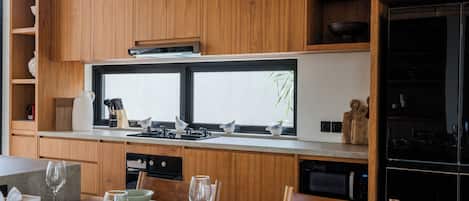 A modern kitchen with wooden cabinets, a large window, and a dining area set for six with a table, chairs, and glassware.