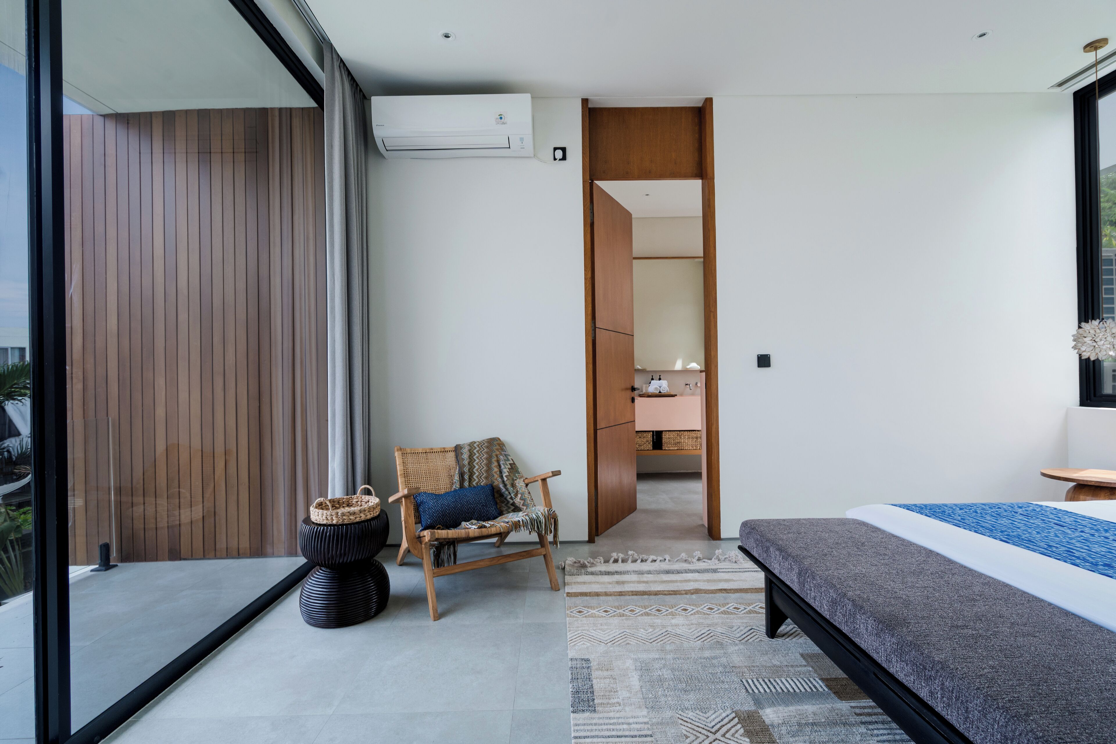 A modern bedroom with a large bed, a chair, a small table, and a view through a glass door.