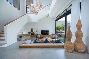 Una sala de estar moderna con un sofá, sillas, una mesa de centro y un televisor. Se ve una escalera que sube a otro nivel.