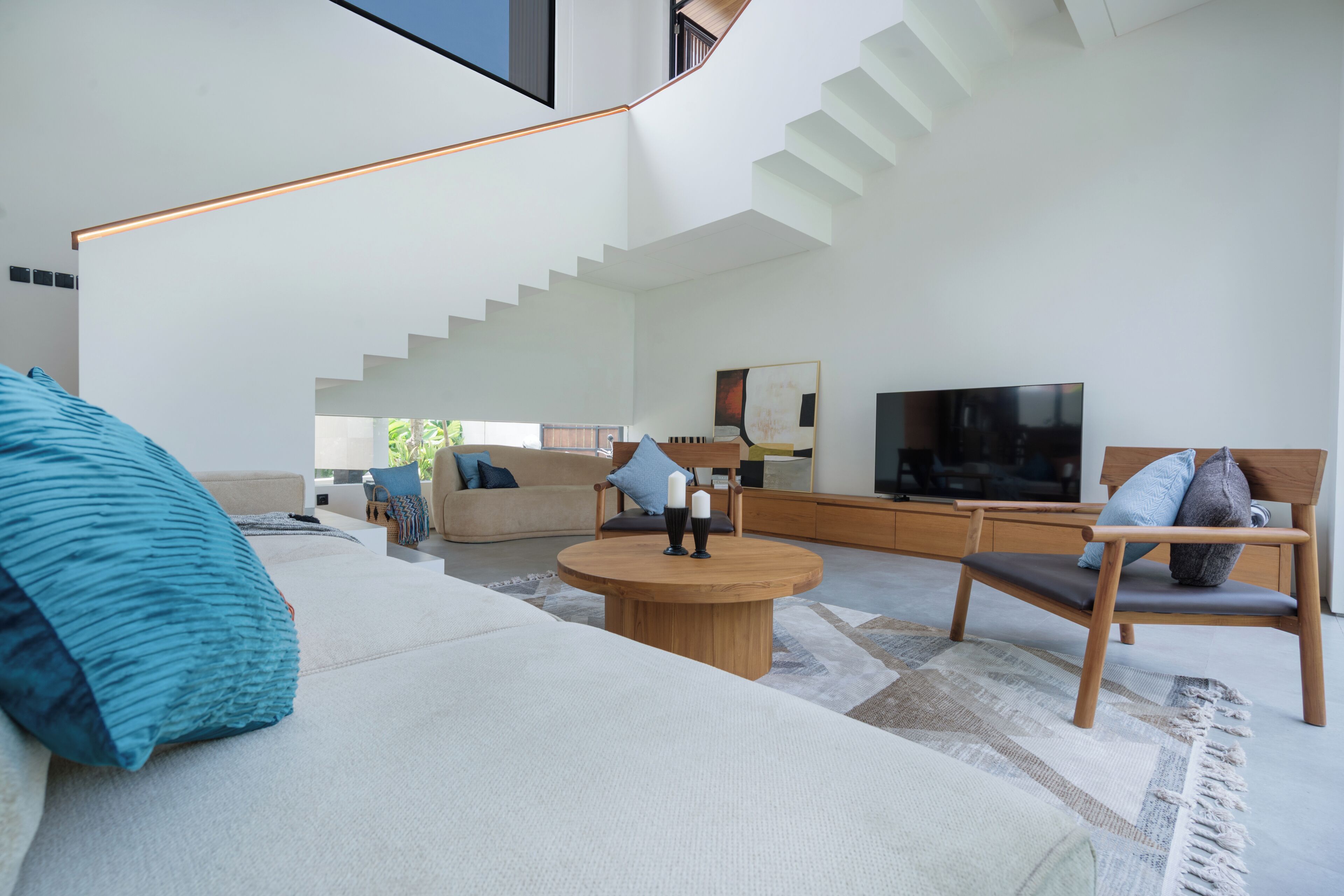 Un salon moderne avec un escalier, une table basse ronde en bois et un grand téléviseur à écran plat.