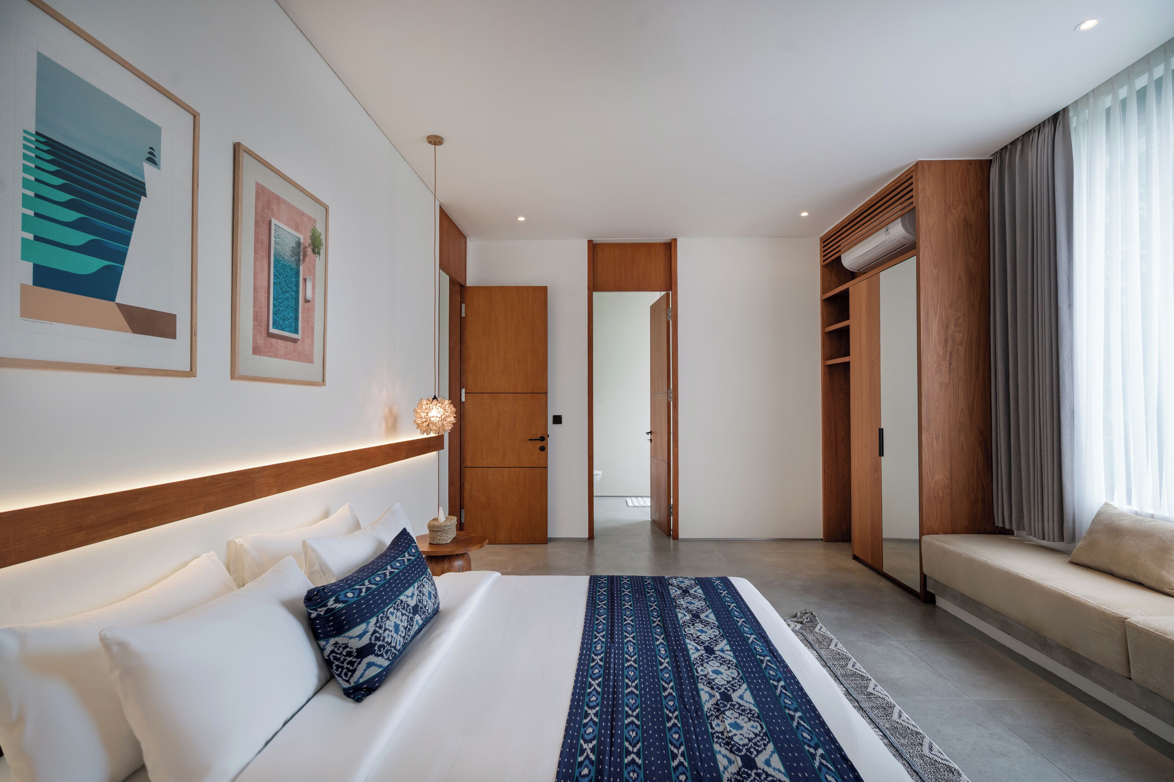 Quarto de hotel moderno com uma cama grande, um sofá, um guarda-roupa de madeira e um corredor que dá para outro quarto.