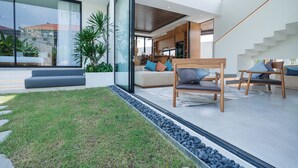 A modern interior with a living area featuring a sofa, chairs, and a glass wall overlooking a garden. - Uma Namu Villa by Betterplace (Canggu)