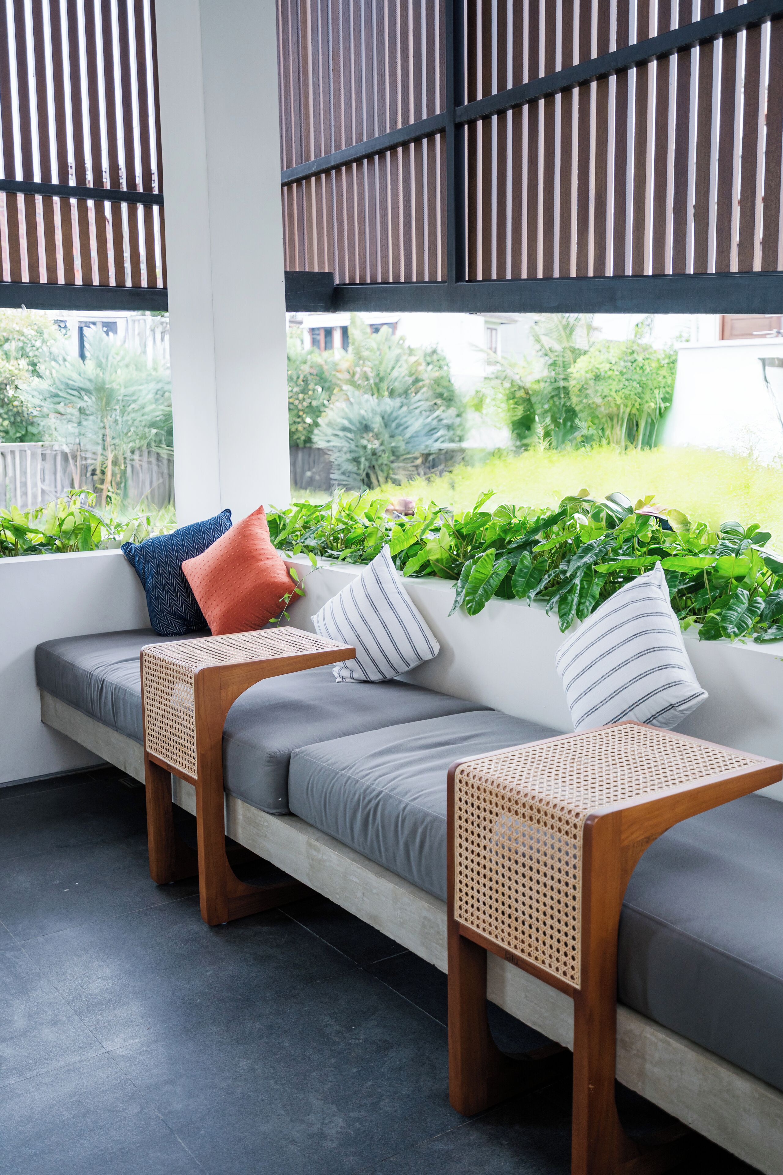 A modern outdoor seating area with a grey sofa, two woven side tables, and a variety of cushions.