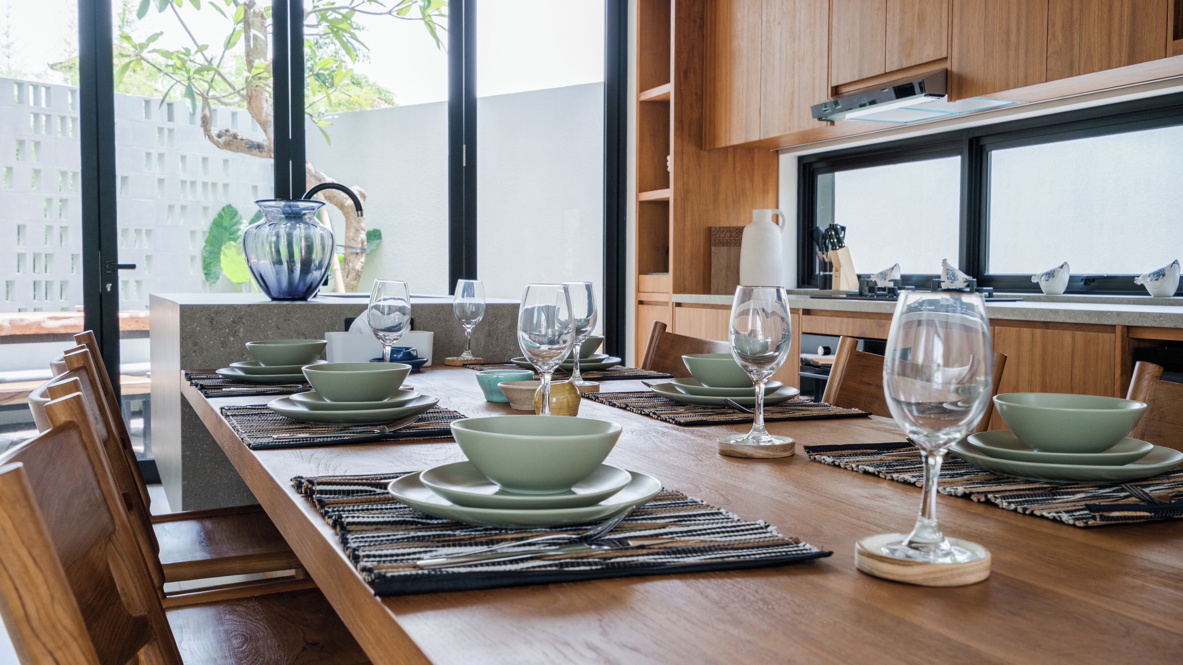 A dining area with a long wooden table set for a meal, featuring green plates and clear glassware.