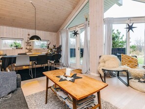 L’intérieur chaleureux d’un chalet comprend un coin repas, un espace salon avec un canapé et un fauteuil, ainsi qu’une grande fenêtre décorée de motifs en forme d’étoiles.