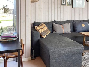 A modern living room with a dark grey sectional sofa, a wooden coffee table, and a small dining table. A stack of books is on the left side of the sofa. - 5 Person Holiday Home in Brovst (Brovst)