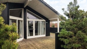 A modern house with a wooden deck, large glass doors, and a covered patio area. - 5 Person Holiday Home in Brovst (Brovst)