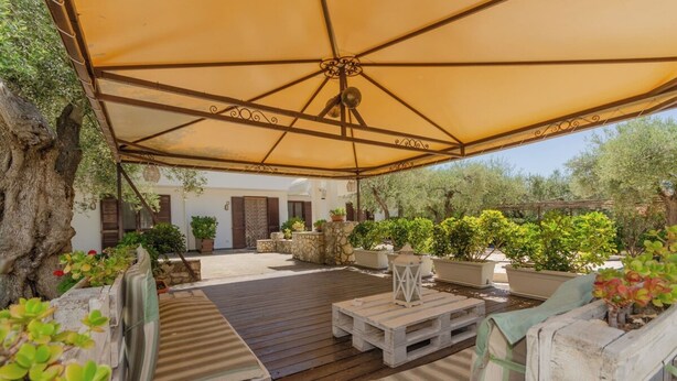 An outdoor patio with wooden furniture, a large canopy, and potted plants. - House The Seagulls - 4. Trilo 6 Sunset (Puglia)