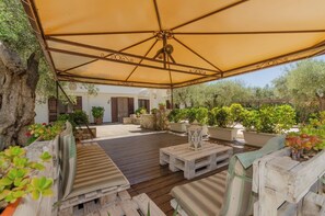 Eine Terrasse im Freien mit Holzmöbeln, einer großen Markise und Kübelpflanzen.