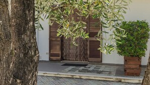 A tree-lined pathway leading to a building with a wooden door and a small potted plant. - House The Seagulls - 4. Trilo 6 Sunset (Puglia)