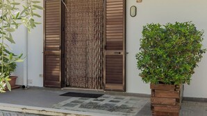 A modern building with a large wooden door, a small potted plant, and a textured wall. - House The Seagulls - 4. Trilo 6 Sunset (Puglia)