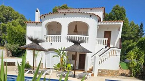 Eine weiße Villa mit Swimmingpool, umgeben von Grün und blauem Himmel.