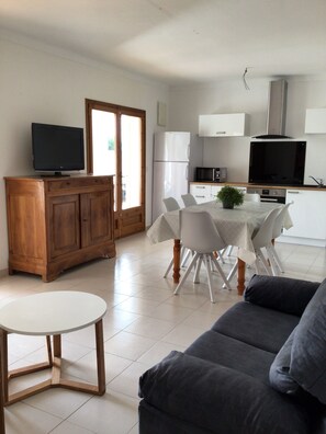 Un salon moderne avec un canapé gris, une table ronde en bois et un coin repas comprenant une table et des chaises blanches.