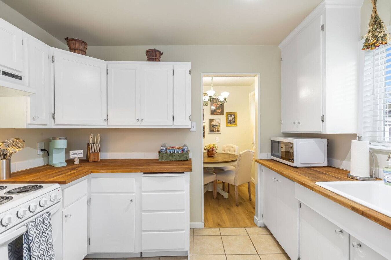 A compact kitchen with white cabinets, a wooden countertop, a stove, and a microwave.
