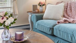 A cozy living room with a teal sofa, a wooden coffee table with a candle, and a lamp on a side table.
