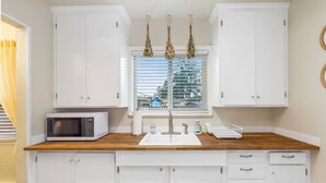 A compact kitchen with white cabinets, a microwave, a sink, and a window with blinds.