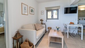 Un salon moderne comprenant un canapé, une table basse en bois, un téléviseur et un petit coin repas avec une table et des chaises.