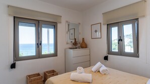 Une chambre à coucher avec un lit, deux fenêtres, une commode, un miroir et une vue sur la mer.