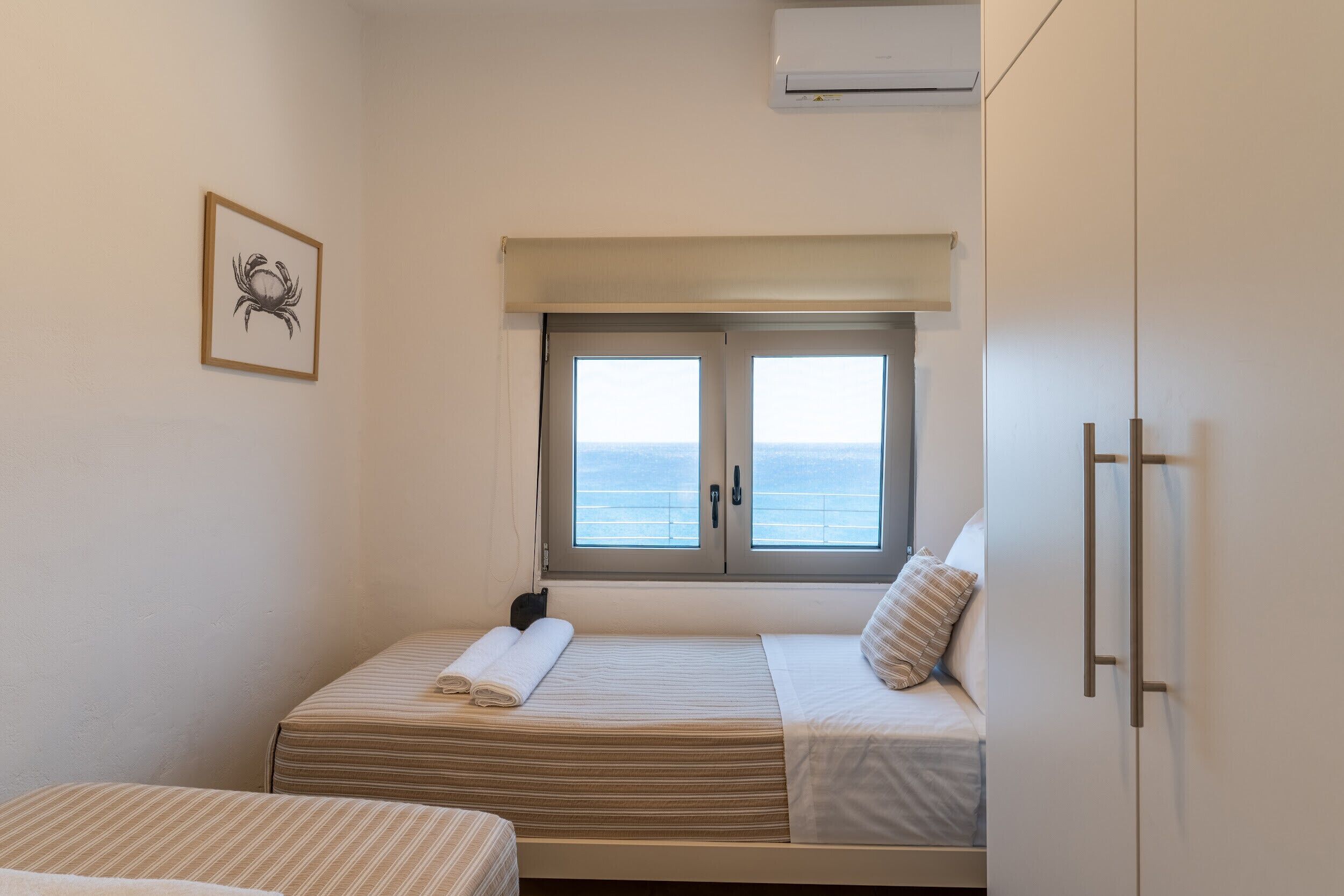 A bedroom with two beds, a window with a view, a framed picture on the wall, and a wardrobe.