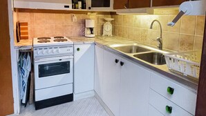 Eine kleine Küche mit weißen Schränken, einem Herd, einem Backofen, einer Spüle und einer Kaffeemaschine.