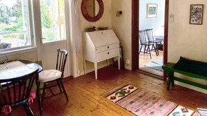 Ein gemütliches Zimmer mit Holzboden, einer weißen Kommode, einem runden Spiegel, einem Esstisch mit Stühlen und einer grünen Bank.