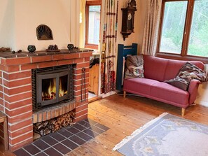 A cozy living room with a brick fireplace, a red sofa, and a window with curtains.