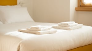 A neatly made bed with folded white towels and a white pillow.