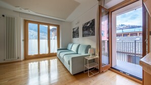 Un salón amplio con un sofá azul claro, una mesita auxiliar y vistas a un paisaje montañoso a través de puertas correderas de vidrio.