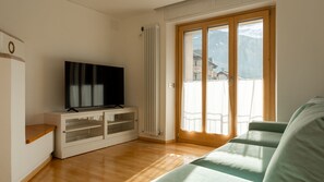 A room with a television on a white cabinet, a sliding glass door leading to a balcony, and a green sofa.