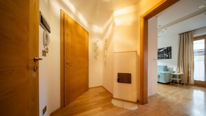 A hallway with wooden flooring, a wooden door, a wall-mounted telephone, and a small white table with a lamp.