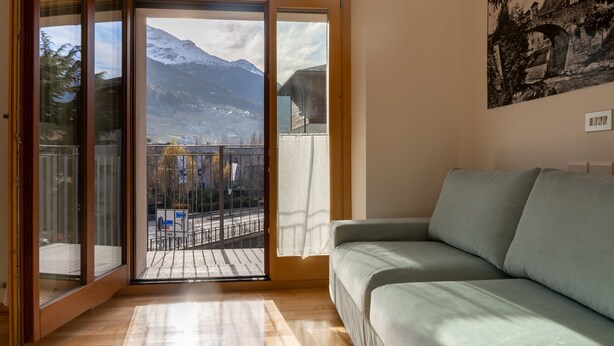 A room with a sliding glass door leading to a balcony with a view of mountains and a town.