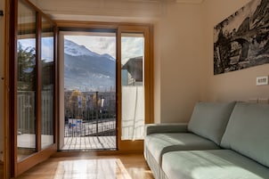Una stanza con una porta scorrevole in vetro che dà su un balcone con vista su montagne e una cittadina.
