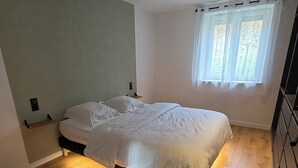 A bedroom with a bed, wooden flooring, a window with curtains, and a nightstand. - At 162 • Cosy 8-person house in the heart of the Vosges mountains (Anould)