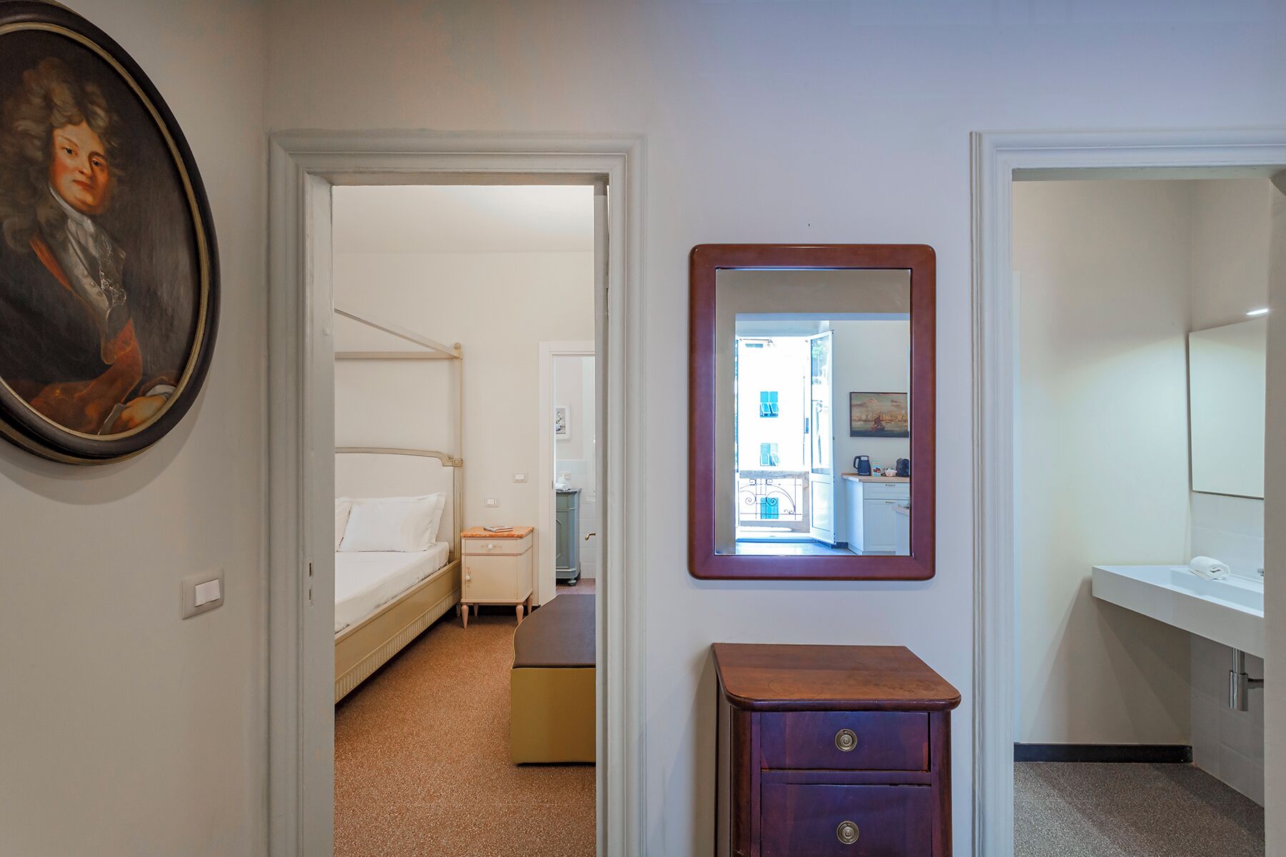 Une chambre d’hôtel avec un lit, une petite armoire en bois, un miroir et un tableau accroché au mur.