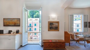 Un espace de vie compact comprenant un coin cuisine, un coin repas et une vue sur un bâtiment par une porte ouverte.