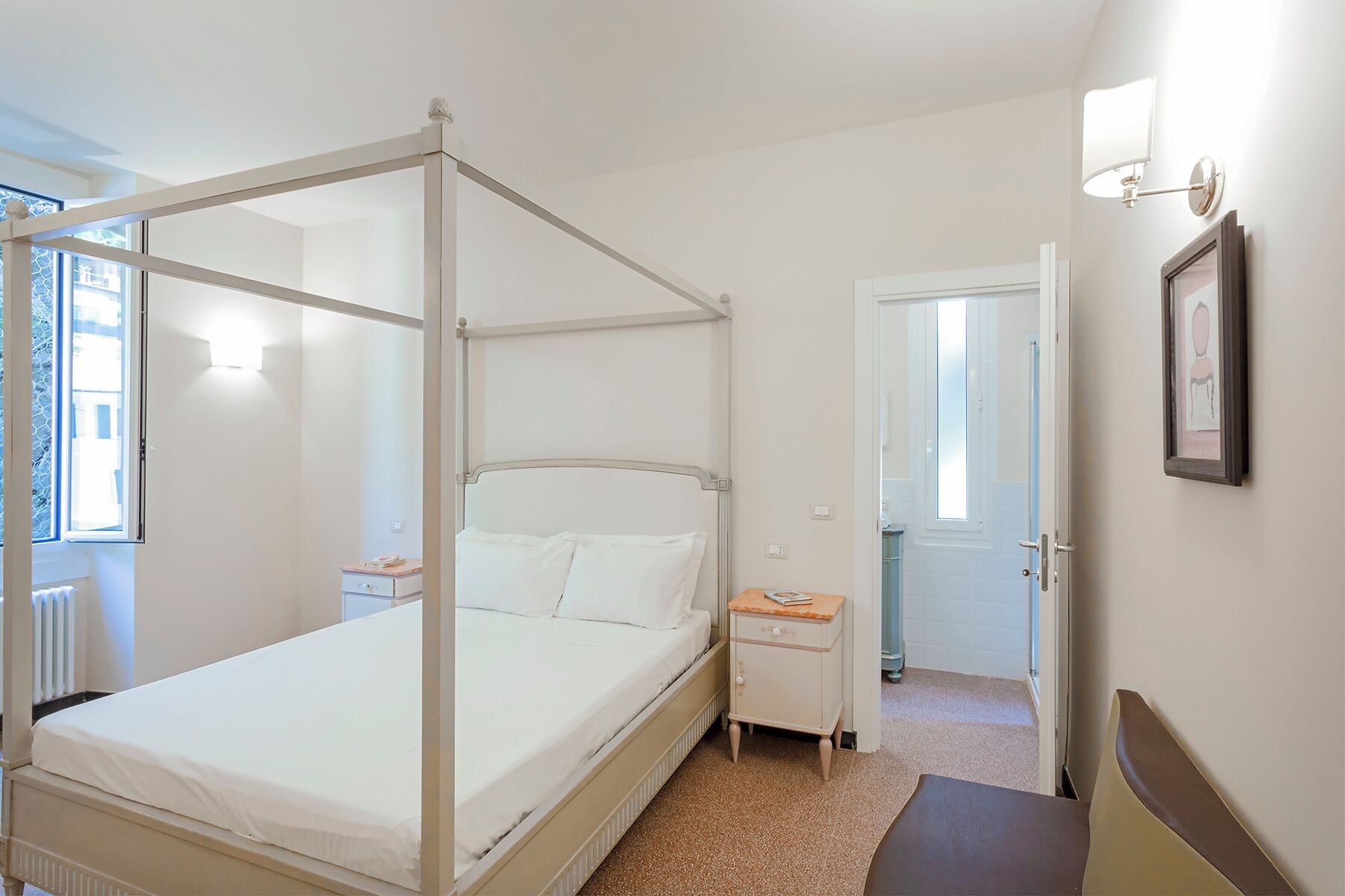 Un lit à baldaquin à quatre poteaux, avec du linge de lit blanc, une table de chevet, une petite commode et un tableau encadré au mur.